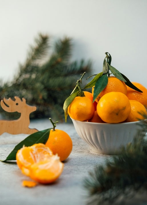 Bowl of mandarins beside a peeled one and a small wooden reindeer decoration