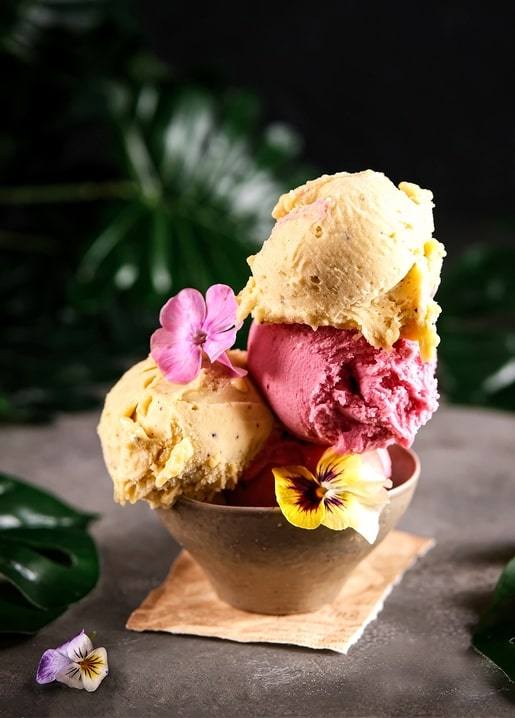 Drei Kugeln Mango-Beeren-Eis in einer Schale mit Stiefmütterchen und Phlox