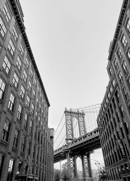 Manhattan Bridge's steel towers framed between tall brick buildings on a Brooklyn street