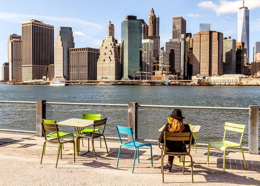 Frau auf bunten Stühlen blickt auf die Manhattan-Skyline vom Brooklyn-Pier