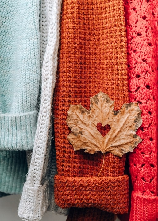 Dried maple leaf with a heart cutout resting on a folded orange knit sweater