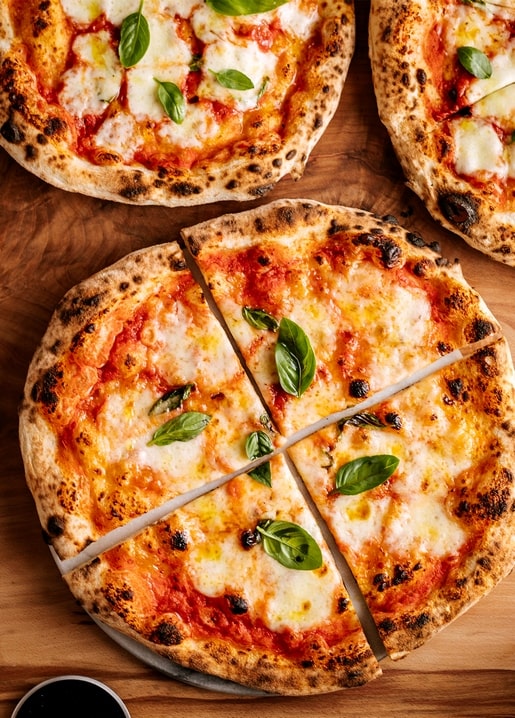 Sliced Margherita pizza topped with basil leaves on a wooden board