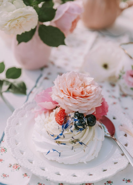 Meringue dessert topped with a pink rose, strawberry, and blueberries on a lace plate