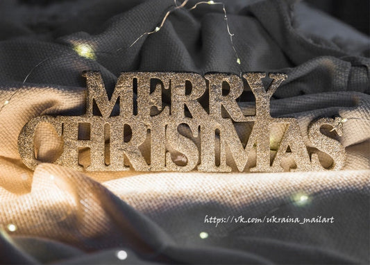 Goldene Glitzerbuchstaben mit dem Schriftzug „Merry Christmas“ auf dunklem Stoff mit Lichterkette