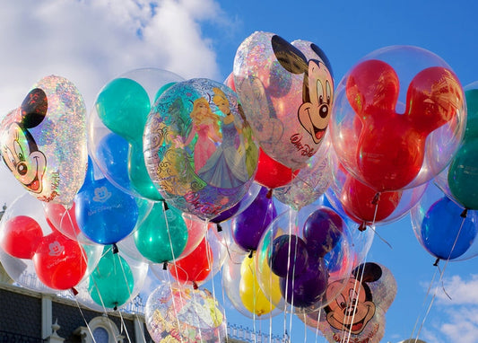 Colorful Mickey Mouse and princess balloons floating against a blue summer sky at Disney World