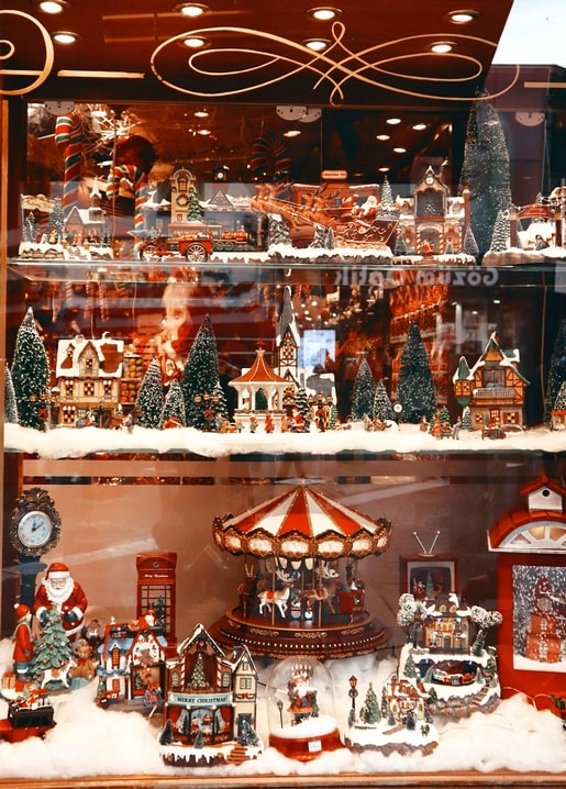 Shop window filled with a miniature Christmas village, carousel, and Santa figures