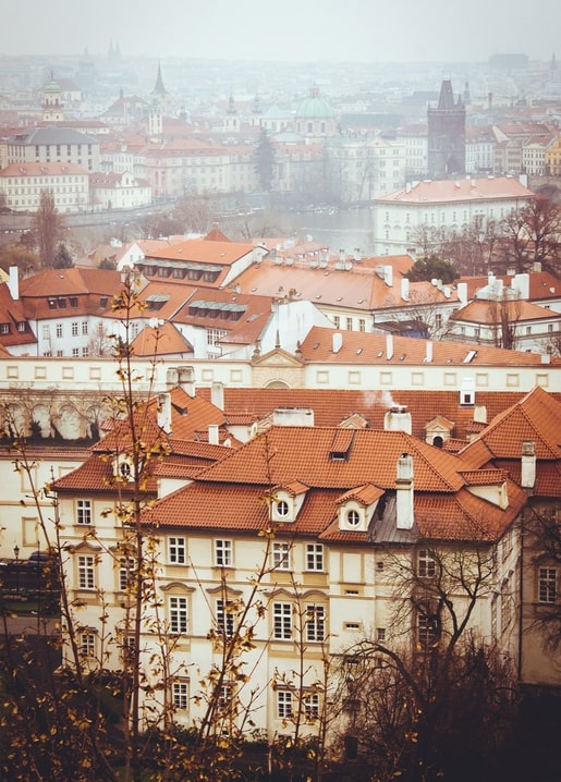 Nebliger Blick von oben auf rote Ziegeldächer und Kirchtürme einer alten europäischen Stadt im Herbst