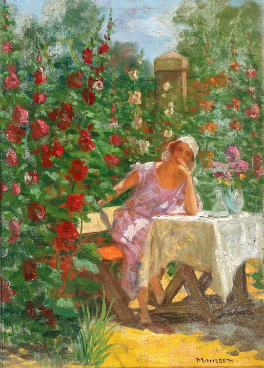 Woman in a floral dress at a garden table surrounded by climbing red and pink hollyhocks