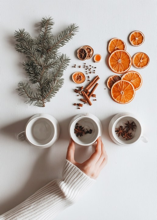 Hand reaching for a mug of spiced tea beside cinnamon sticks, star anise and dried orange slices