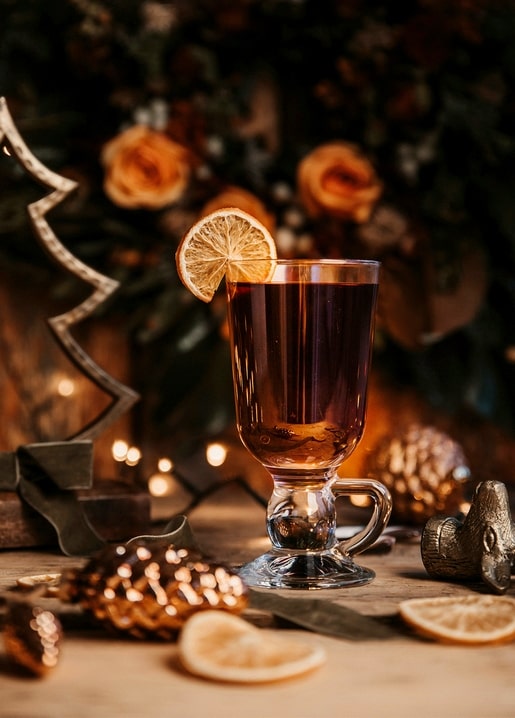 Mug of mulled wine with orange slice among pinecones and fairy lights