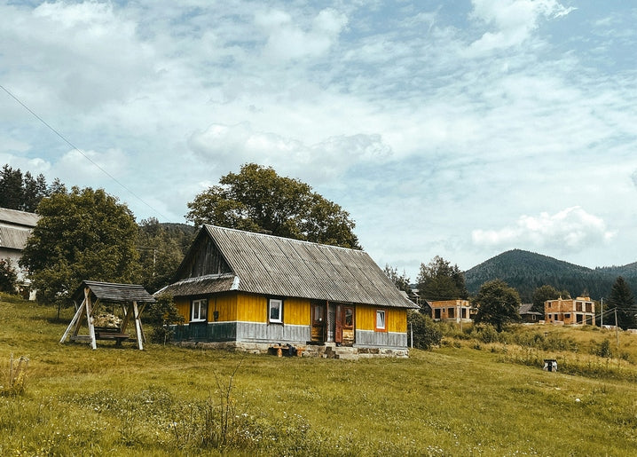 Yellow wooden house with a tin roof in a Carpathian meadow near Mykulychyn, mountains behind