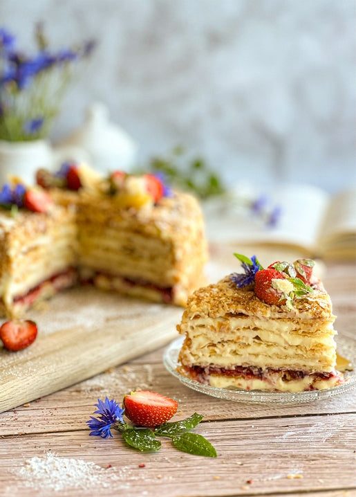 Slice of layered Napoleon cake with strawberries and blue cornflowers