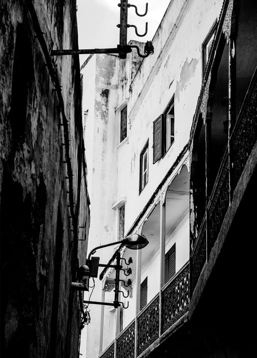 Narrow old-town alley with whitewashed walls and a wrought-iron balcony overhead