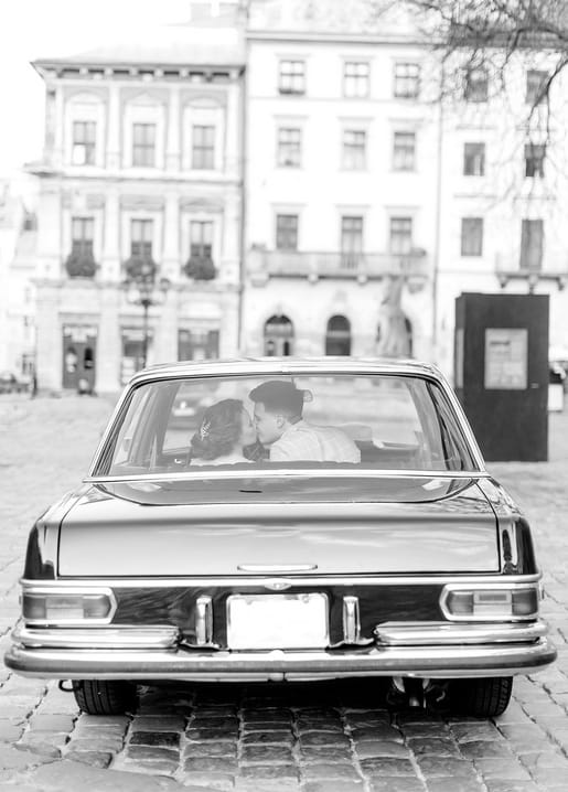 Brautpaar küsst sich auf dem Rücksitz eines Oldtimers, Schwarzweißfoto