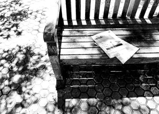 Folded newspaper on a weathered wooden bench with dappled light and hexagonal paving stones