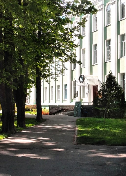 Sunlit chestnut alley leading to NUBiP's green-and-white Agrobiology Faculty building