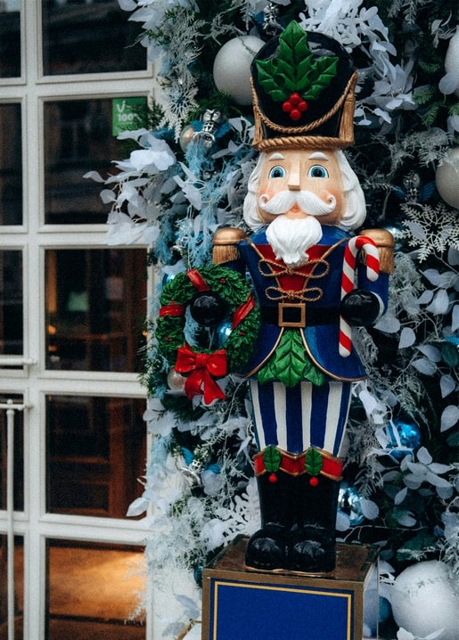 Wooden nutcracker soldier holding a candy cane and wreath by a frosted Christmas tree