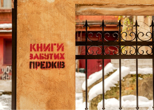 Red stenciled lettering on an ochre wall behind a wrought-iron gate in Lviv