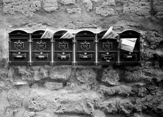 Black-and-white photo of six antique mailboxes set into a stone wall, letters inside