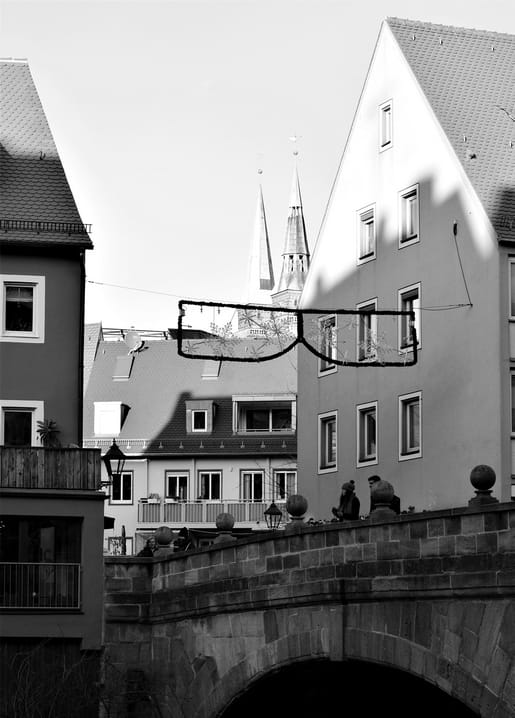 Schwarzweißaufnahme einer Steinbrücke und Altstadt mit zwei Kirchtürmen im Hintergrund