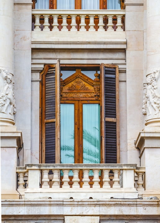 Ornate stone balcony with dark wooden shutters and carved sculptural figures