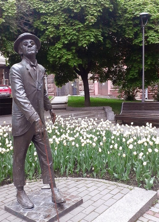 Bronze statue of Panikovsky with cane and hat beside a bed of white tulips, Kyiv park