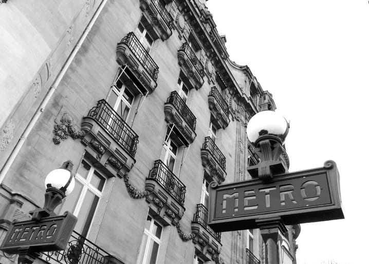 Verzierte Haussmann-Fassade mit Balkonen neben einem Pariser Metro-Schild, Schwarz-Weiß