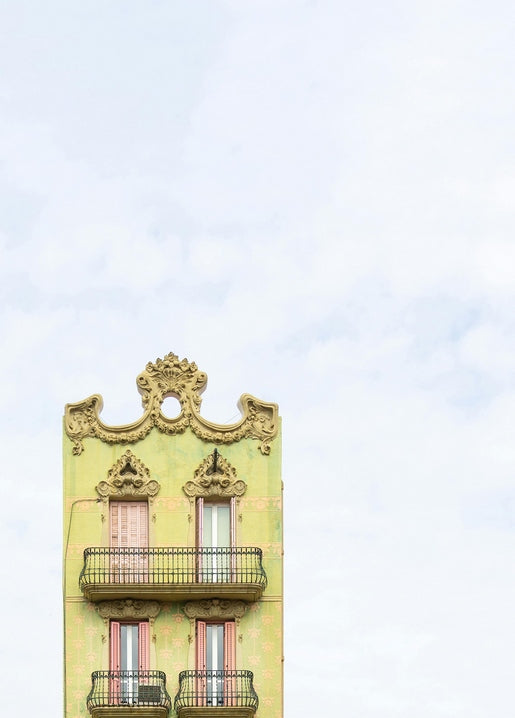 Ornate pastel-yellow Art Nouveau building facade with wrought-iron balconies against a pale sky.