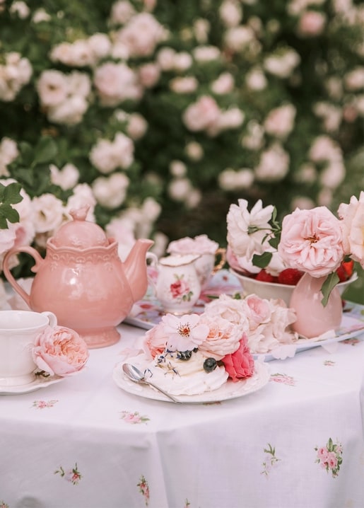 Pink teapot and pavlova cake topped with roses and berries on a garden table