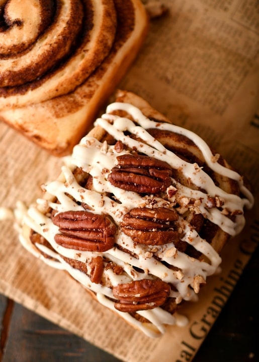 Zimtschnecke mit Frischkäseglasur und Pekannüssen auf Pergamentpapier