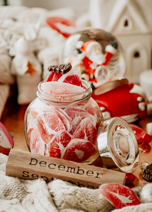 Glass jar of peppermint candies beside a Santa snow globe and a wooden “December” block