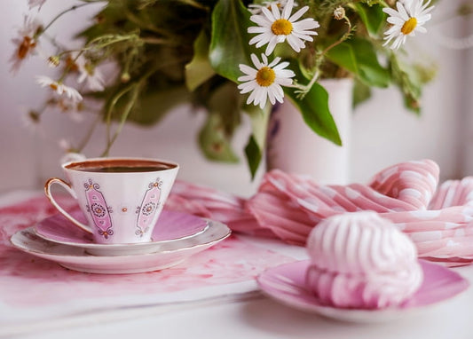 Pink porcelain coffee cup, a fluffy marshmallow and a bouquet of white daisies