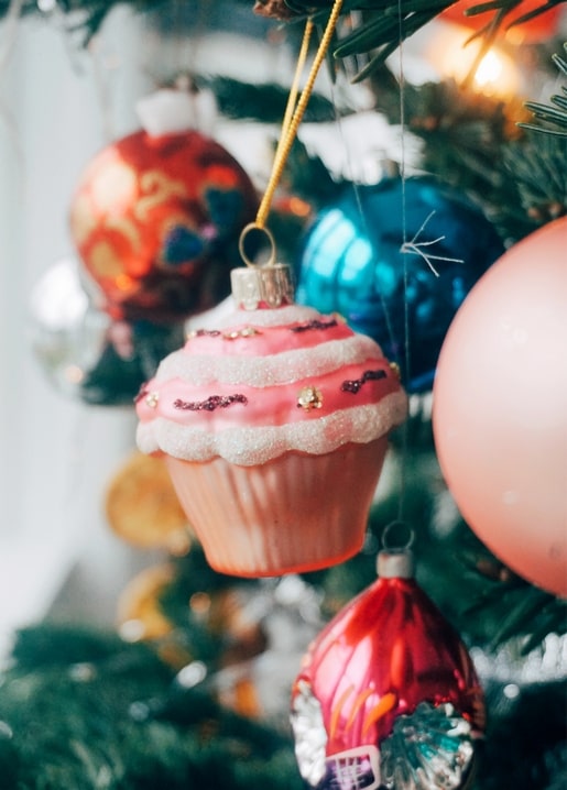 Glittery pink cupcake-shaped bauble hanging on a Christmas tree with red and teal ornaments