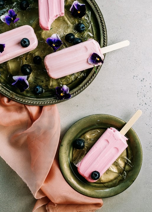 Rosa Eis am Stiel auf einem Tablett mit Eis, Blaubeeren und Veilchen