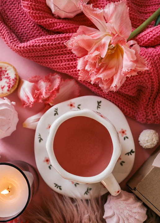 Pink tulip on a knitted blanket beside a floral teacup and lit candle