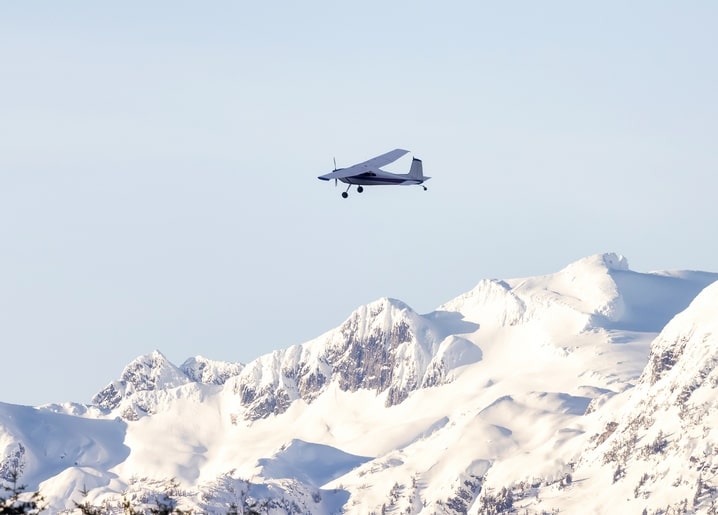 Small propeller plane flying over snow-covered mountain peaks