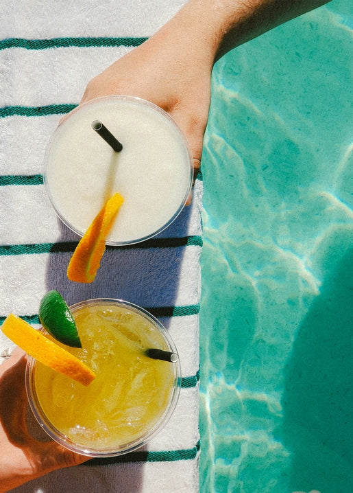 Two cocktails with citrus garnish held poolside on a striped towel