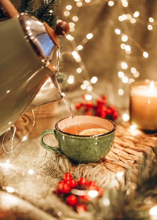 Tea pouring from a kettle into a green mug beside a candle and red berries