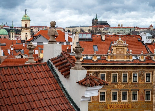 Rote Ziegeldächer und Steinfiguren vor Prags Altstadt unter bewölktem Herbsthimmel