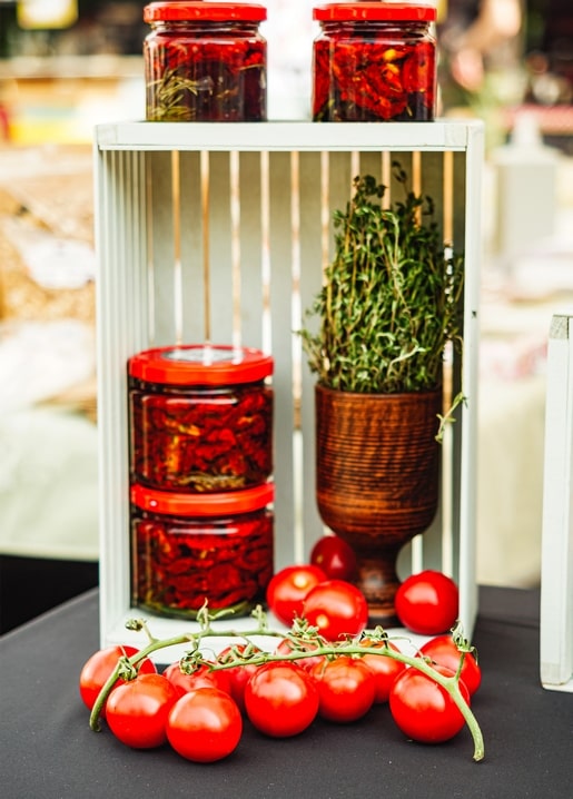 Gläser mit eingelegten Tomaten und Thymian in einer Holzkiste mit frischen Tomaten
