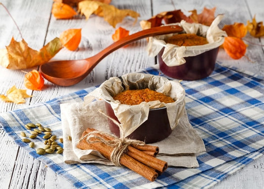 Pumpkin muffin in a paper-lined ramekin with cinnamon sticks and a wooden spoon on plaid cloth