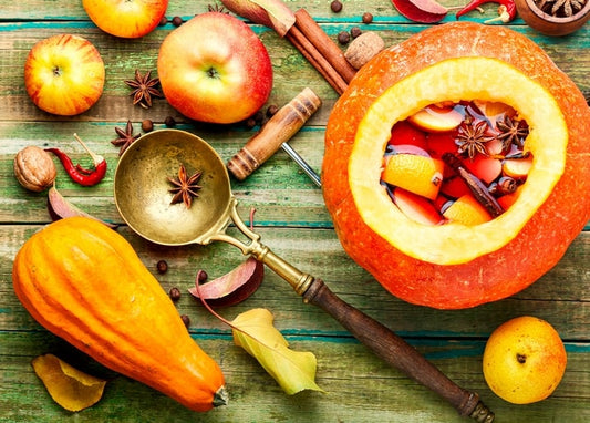 Ausgehöhlter Kürbis mit Glühwein neben Äpfeln, Zimt und Sternanis