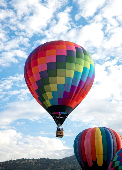 Colorful patchwork hot air balloon rising into a blue sky above green hills