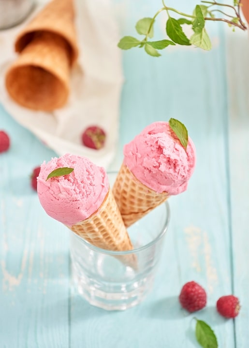 Zwei Himbeer-Eiswaffeln im Glas mit Minze und verstreuten Himbeeren