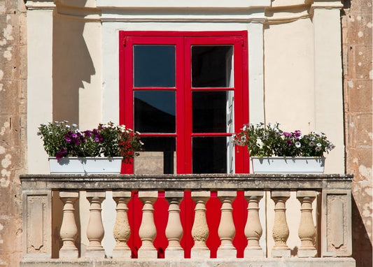 Red-framed balcony door with purple and white petunias in white planters