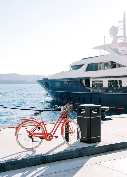 Red bicycle parked on a pier next to a white yacht in a marina
