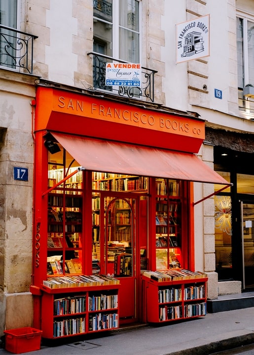 Red-fronted Parisian bookshop with books displayed in crates under a striped awning