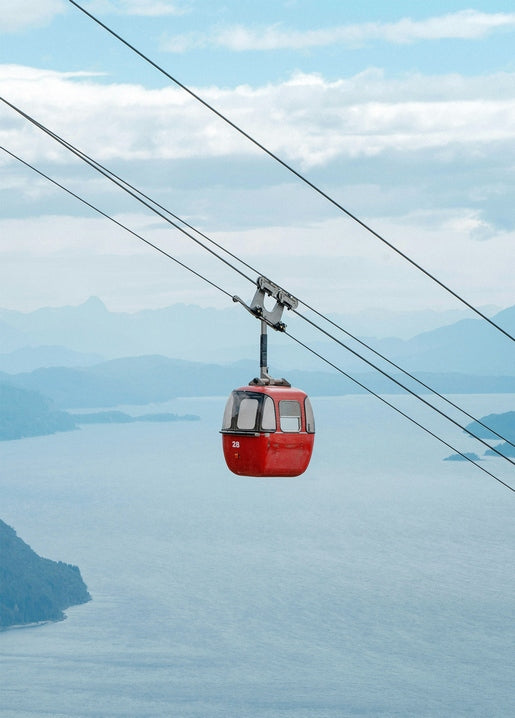 Red cable car gondola suspended over a coastal view of sea and misty mountains