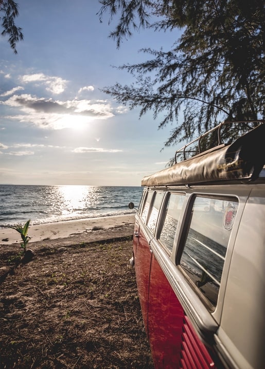 Red and white camper van parked on the beach at sunset
