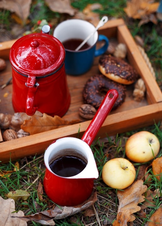 Rote Emaille-Kaffeekanne, Schokoladendonut und Äpfel auf einem Herbst-Picknicktablett